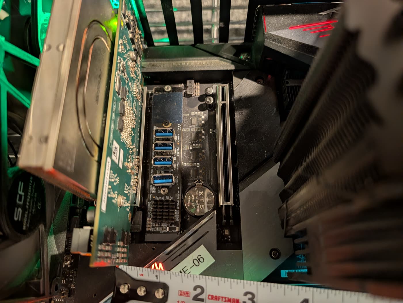 Looking down into aifoundry2: the ET card on the left with its parts-covered back facing right, an empty steel-armoured PCIe x16 slot in the middle, the CPU cooler's fins on the right, an M.2 adapter board and a coin battery between them, a measuring blade along the bottom.